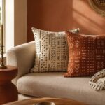 DIY mudcloth pillow covers in cream and rust styled on an oat-linen sofa with folded throw
