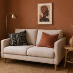 Afro-boho decor on a budget — small sofa with mudcloth and terracotta pillows, rattan side table, framed portrait, brass lamp